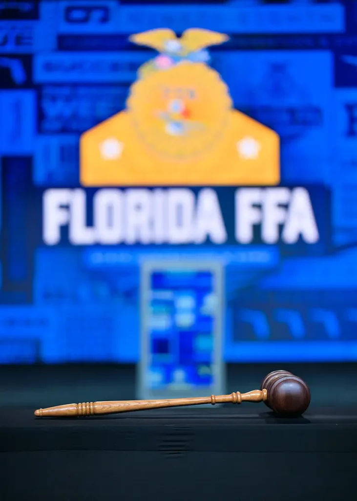 A wooden gavel rests on a table with a blurred background showing the words "FLORIDA FFA" and a yellow emblem on a blue backdrop.